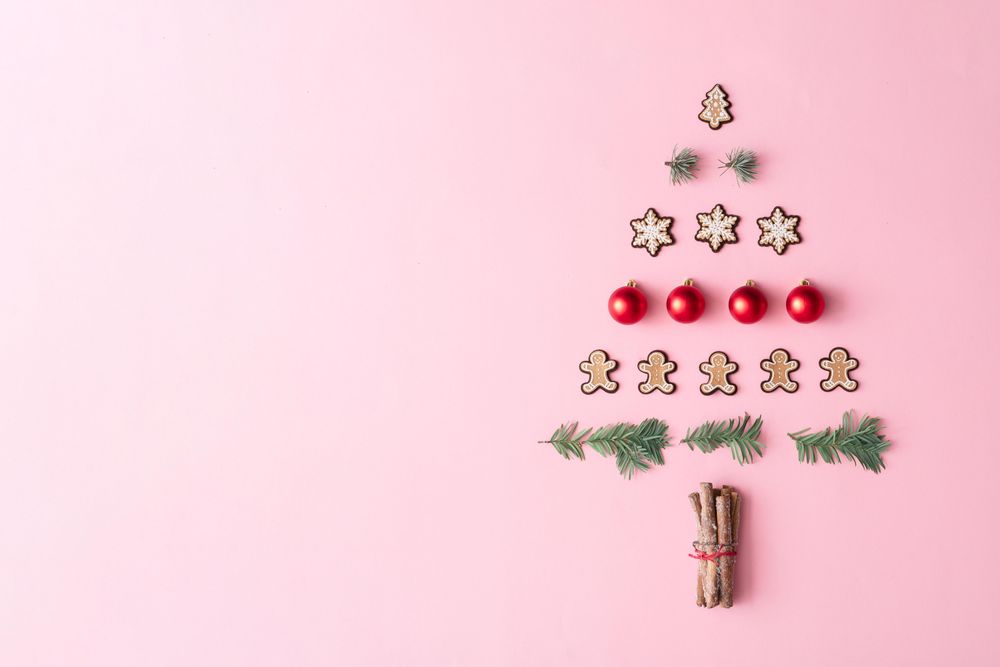 Christmas tree made with evergreen fir, bauble decoration and winter cookies on pink background