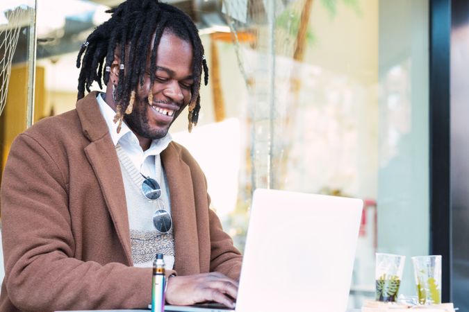 Happy Black man browsing on laptop on restaurant terrace