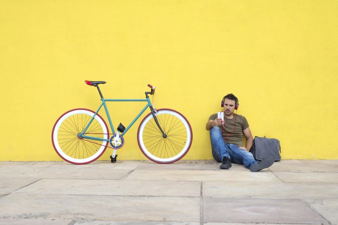 Man sitting in front of yellow wall with bike listening to music