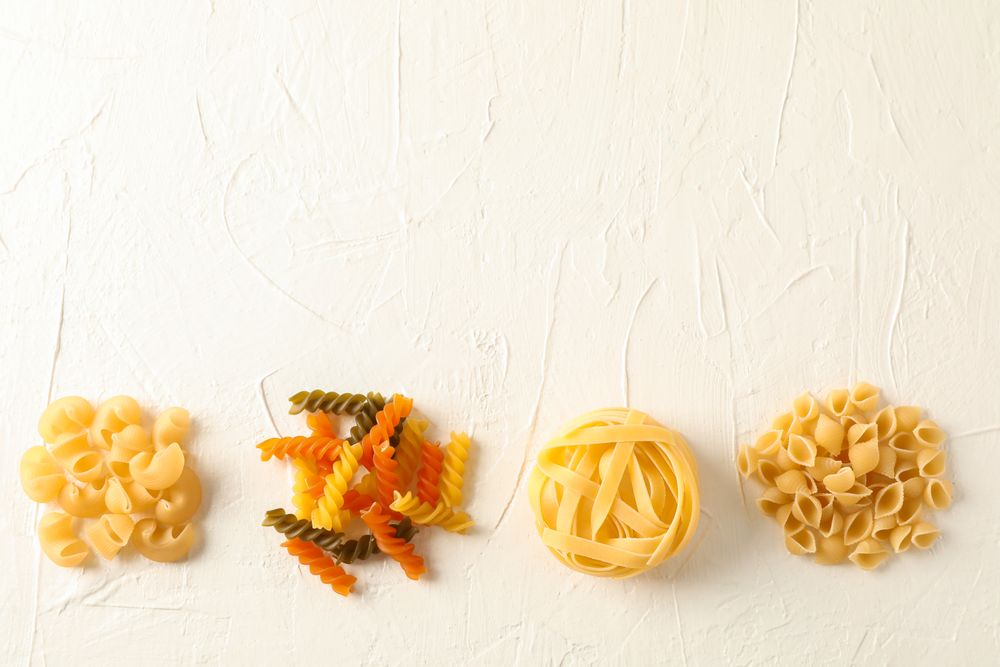 Flat lay composition with different pasta on light background, space for text. Dry uncooked whole pasta