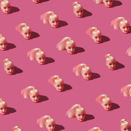 Pattern made of doll heads on pink background