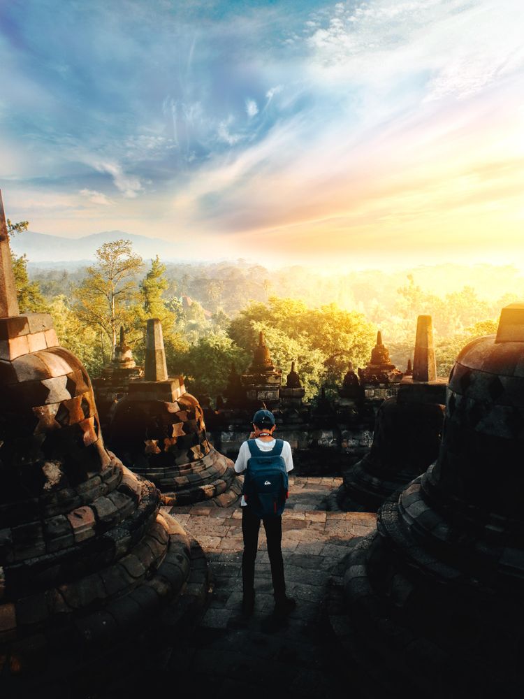 Back view of young man with backpack standing beside ruins
