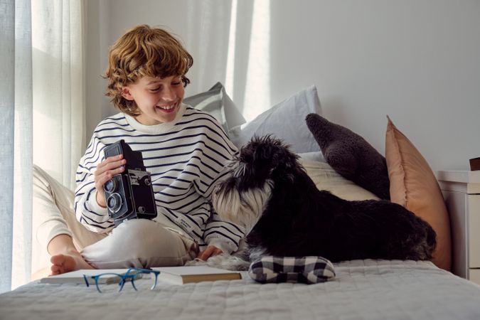 Glad schoolboy with retro photo camera and dog on bed