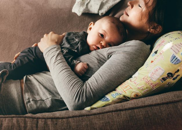 Mother taking rest sleeping on a couch with her baby on her chest