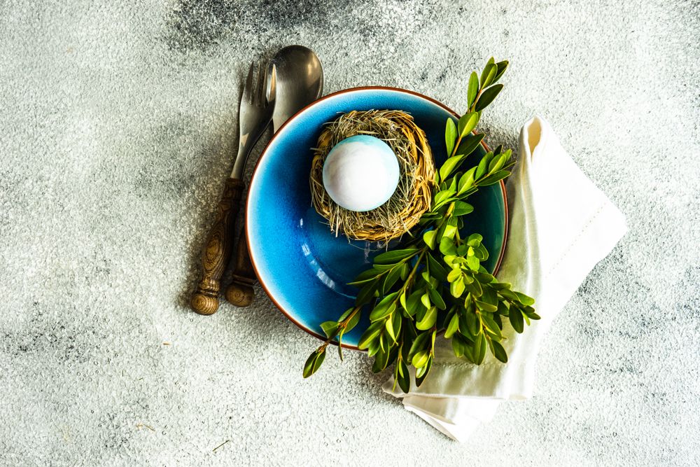 Top view of Easter table setting with blue bowl with decorative egg in nest with copy space