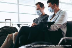 Couple sitting at airport with face mask using smart phone 48PVR4