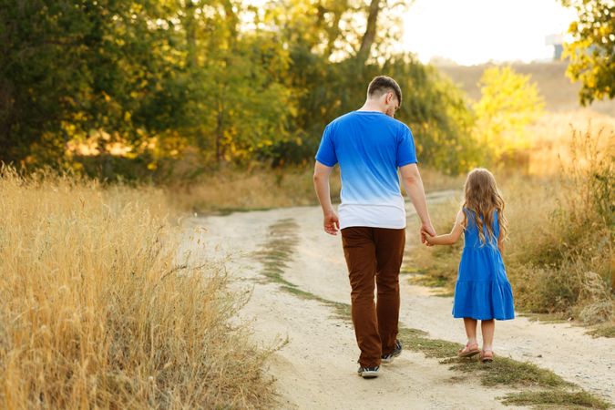 Man and daughter dressed in blue walking along forest road