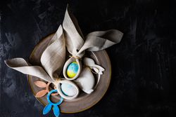 Easter eggs wrapped with rabbit ears with napkin with nest on dark table