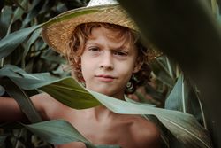 Charming boy in straw hat among green leaves