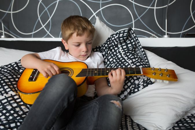 Young blonde boy playing toy guitar