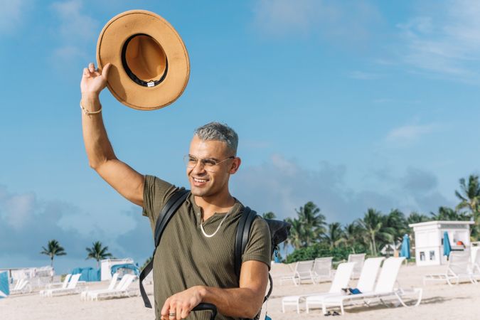 Young man waving to someone with his cowboy hat, seated on his carrying luggage.
