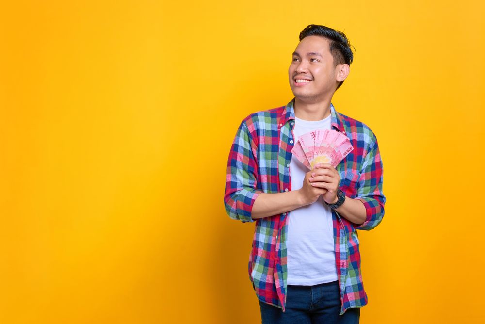 Asian man holding cash with both hands and looking away in studio shoot