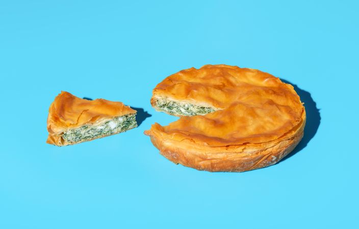Phyllo dough savory pie with spinach and cheese, isolated on a blue background