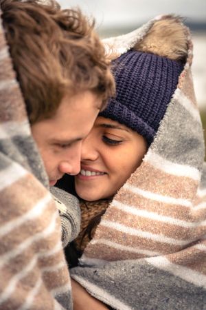 Close up of couple cuddling while wrapped in blanket on a windy day, vertical