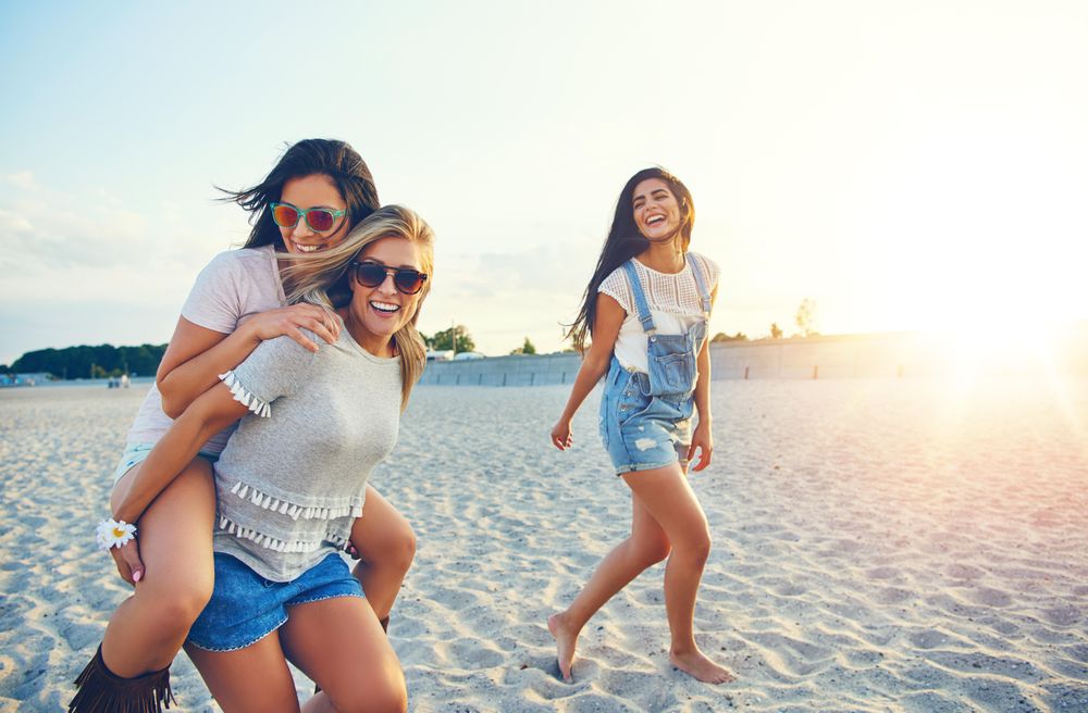Three happy friends having fun walking on sand at the beach