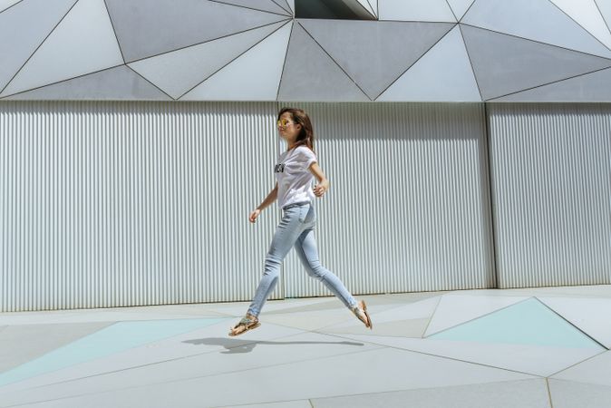 Cheerful woman jumping near modern wall