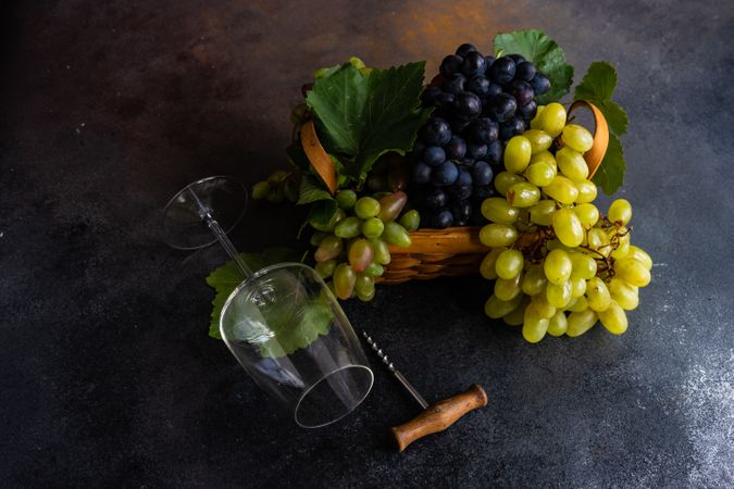 Box of fresh green & red grapes on grey kitchen counter with wine glass