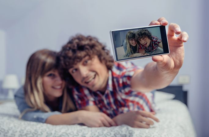 Screen of couple in love taking selfie with smartphone on bed