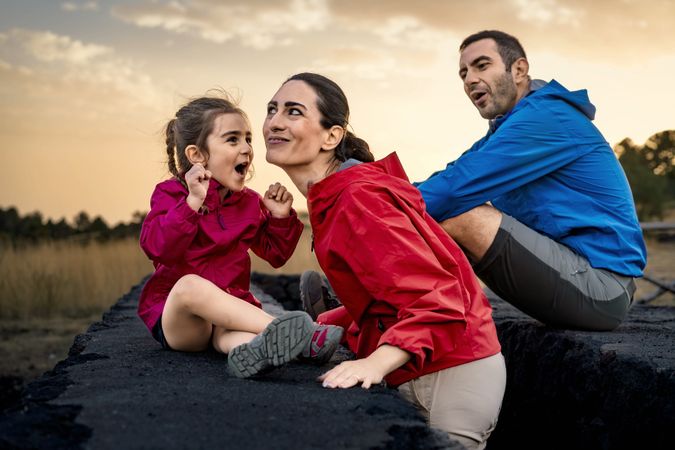 An excited child telling a story to her mother during a family hike at sunset.