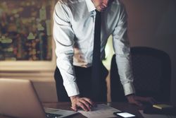Focused man standing over documents and laptop