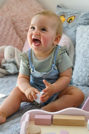 Cheerful baby playing with toy on bed