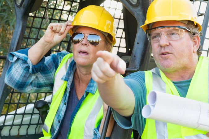 Male and Female Workers With Technical Blueprints Talking at Construction Site