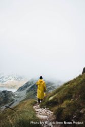 Back view of a person in yellow raincoat standing on top of a mountain 5XJyGb