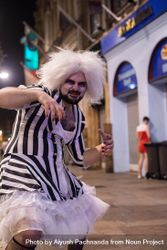 Young man partying in street wearing Beetlejuice tutu drag costume in Halloween monster pose 5XrR7b