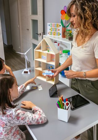 Teacher explaining to her students the parts of a sustainable house showing an electric car