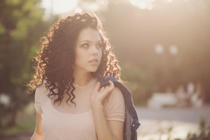 Young woman looks to her side outside while holding coat over shoulder