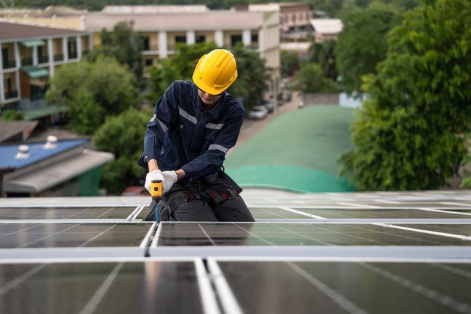 Engineer worker using electric drill repairing on solar cell panel on the roof of the factory. After service and security for industrial renewable energy concept