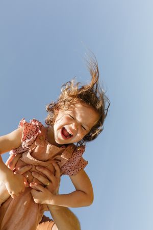 Happy anonymous holding playful daughter against cloudless sky