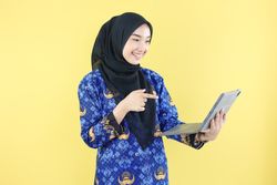 Cheerful Muslim  Woman in Blue Korpri Batik Uniform pointing at Laptop