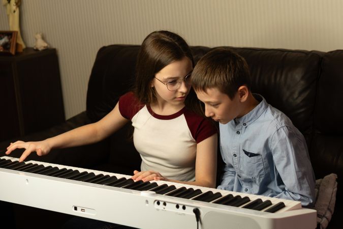 Girl teaching boy to play the keyboard at home.