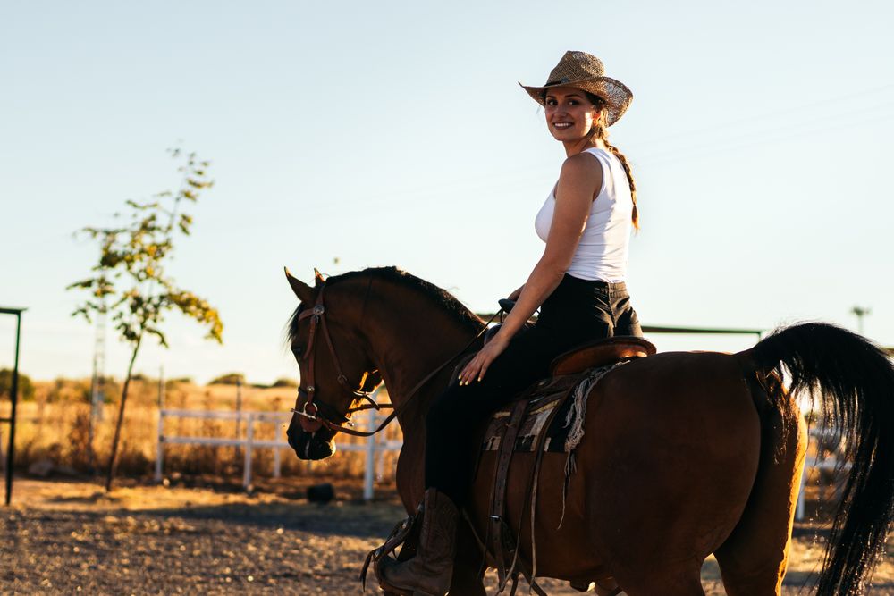 Young woman in hat riding a horse in the countryside at sunset