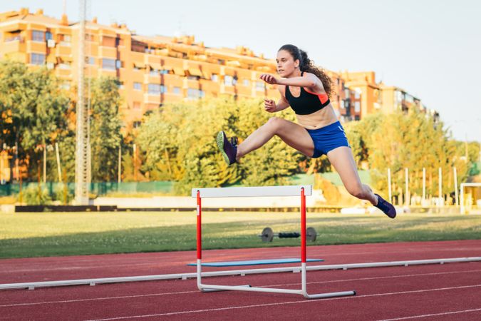 An athletic woman jumping hurdles on an athletics track.
