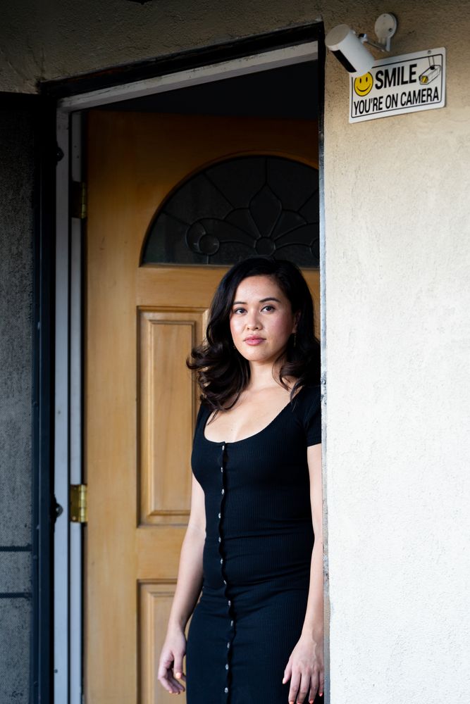 Woman looking seriously at camera leaning against her doorway at home