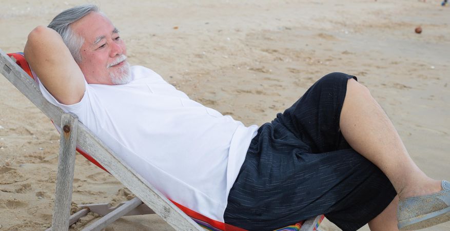 Older Asian male relaxing on beach chair in the sand