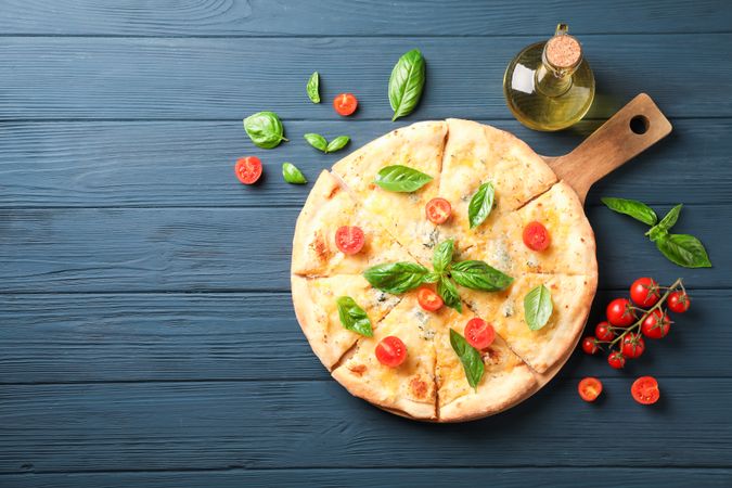 Cheese pizza, tomatoes and olive oil on wooden background, copy space