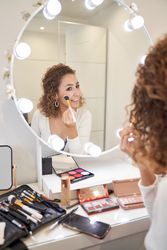 Smiling young female applying makeup on cheeks with brush