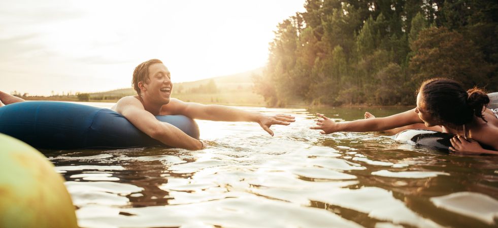 Loving young couple about to hold hands on innertubes on lake
