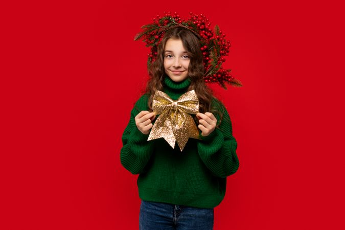 Young girl in green sweater holding large golden glittery bow