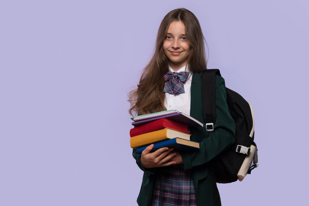 Schoolgirl holds stack of books while posing confidently.