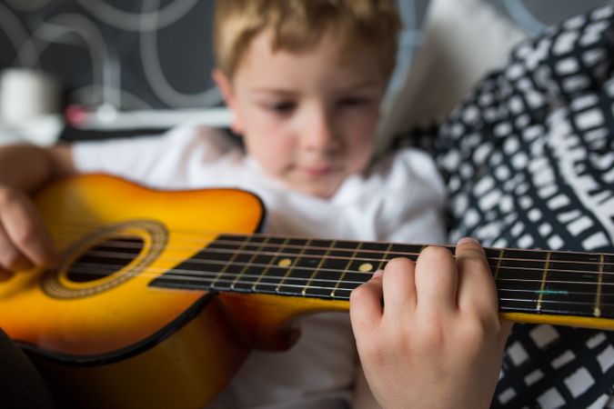 Young blonde boy playing toy guitar