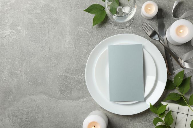 Composition of table setting with candles, leaves and cutlery on gray background