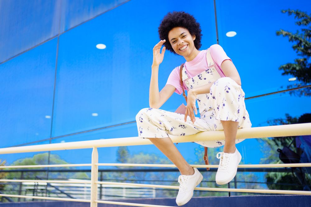 Happy woman sitting on handrails in front of reflective building