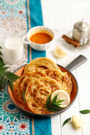 Skillet of roti served with citrus, tea and milk