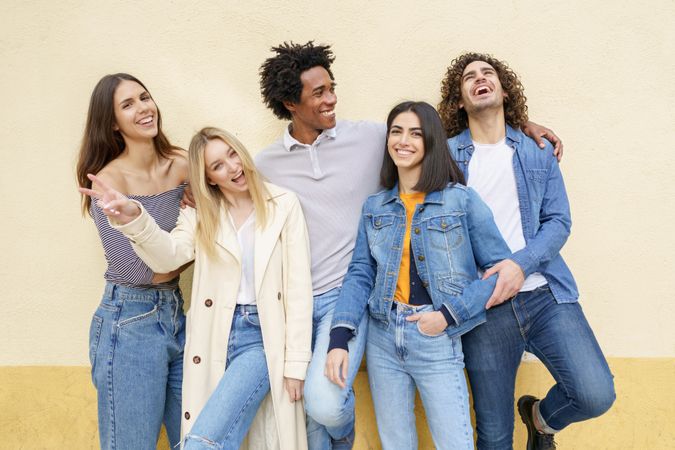 Smiling friends posing for picture leaning against a yellow wall
