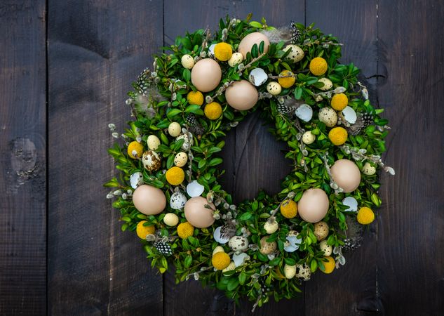 Easter card concept with fresh wreath with decorative eggs and feathers hanging on door