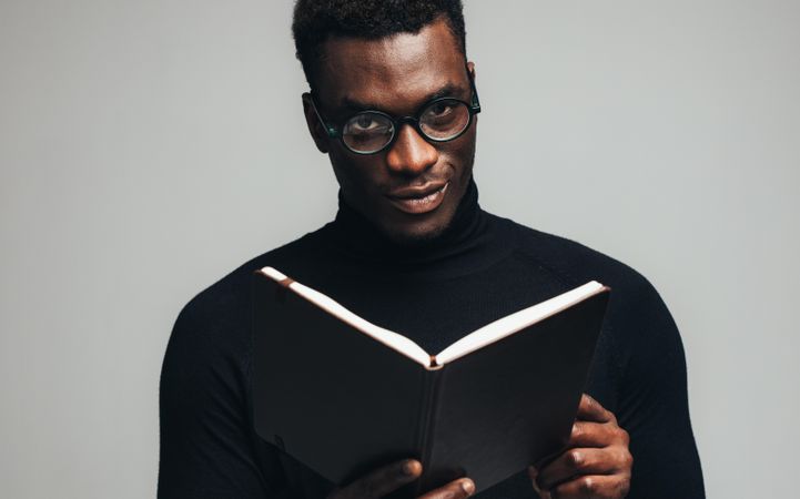 Black man looking at camera with a book in hand